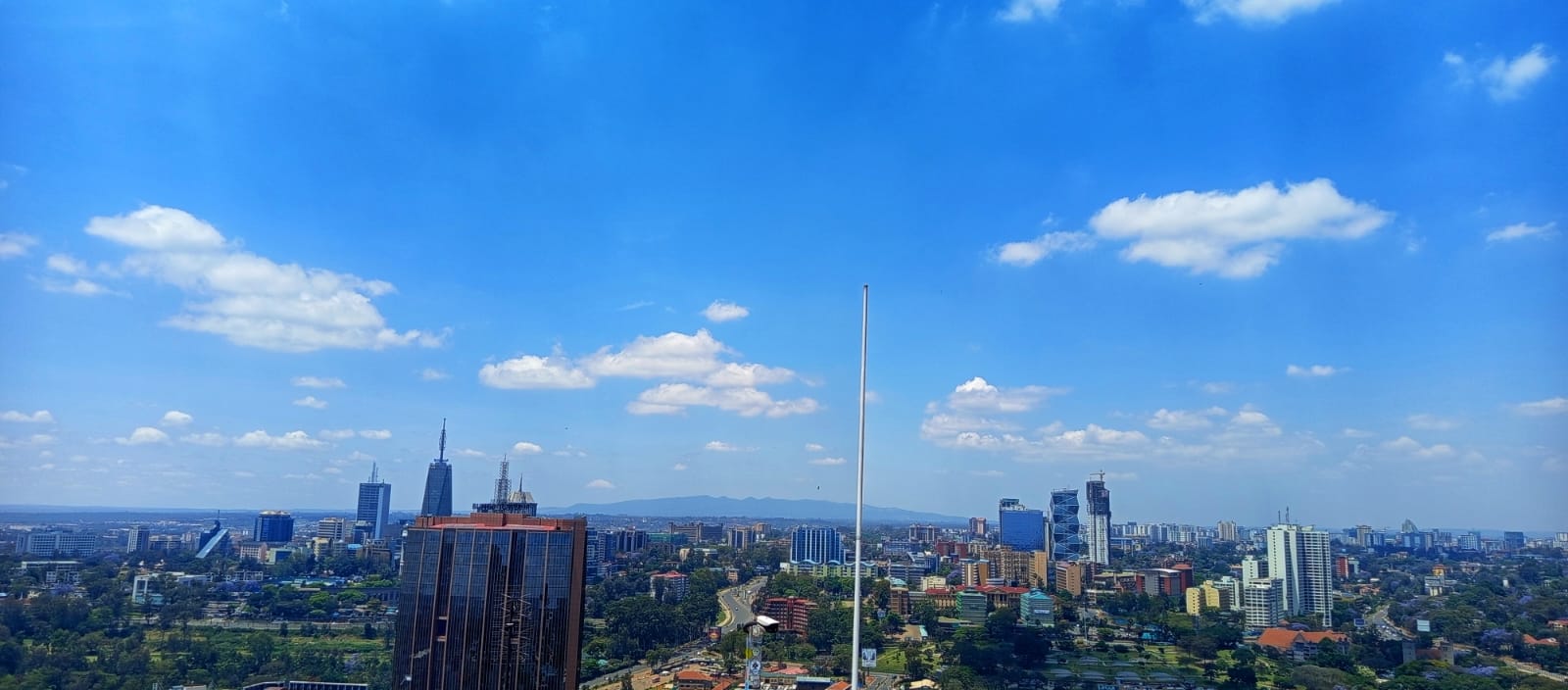 Shows the wide expanse of the city under a brilliant blue sky, with the iconic UAP Old Mutual Tower visible in the distance.