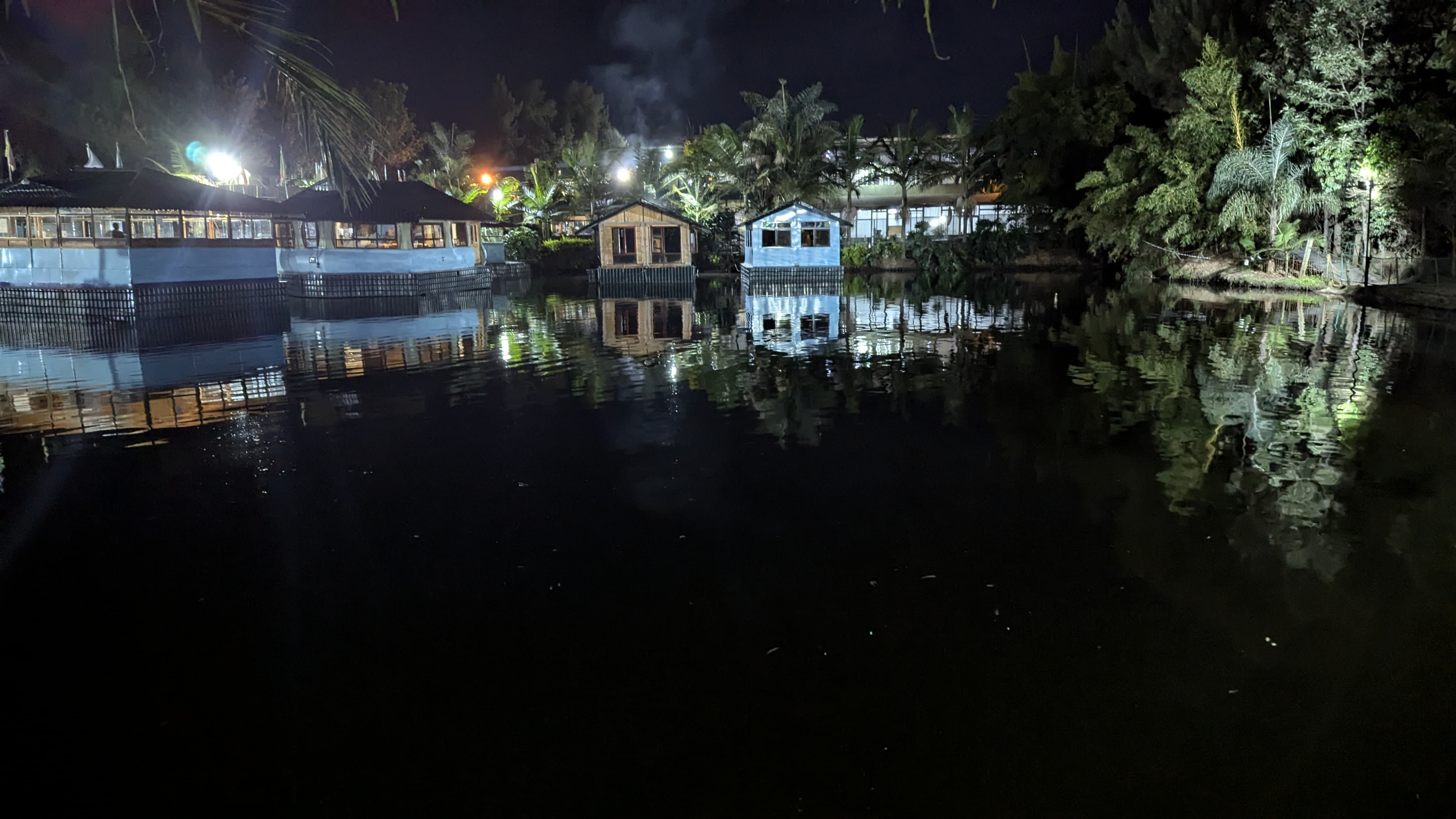 A beautiful night shot of a waterfront restaurant. Small, lit-up wooden cabins are built right over the water, creating perfect reflections on the dark surface.